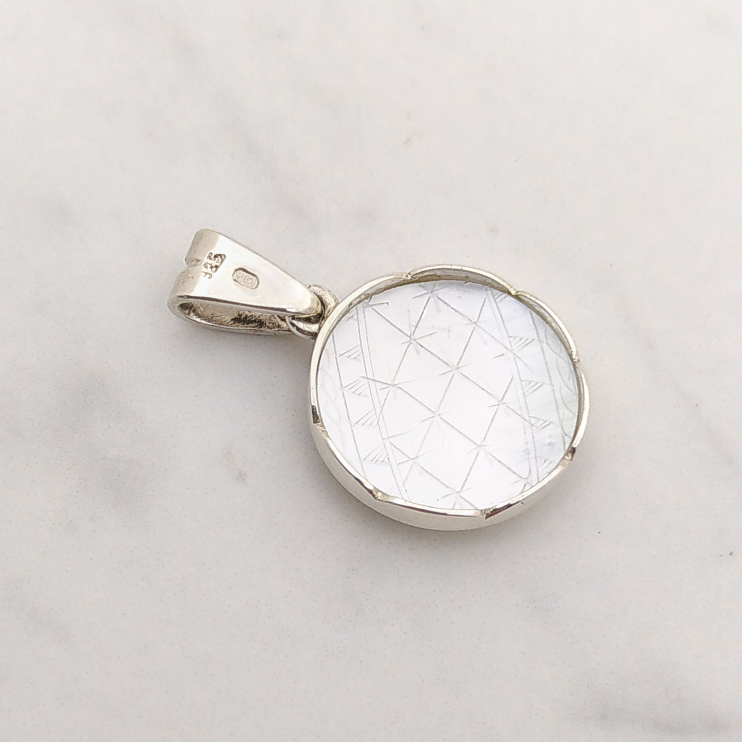 This picture shows the back of the Marguerite pendant. A rond mother of pearl disc is set in silver, and one can see engraved lines forming a thin geometric pattern.