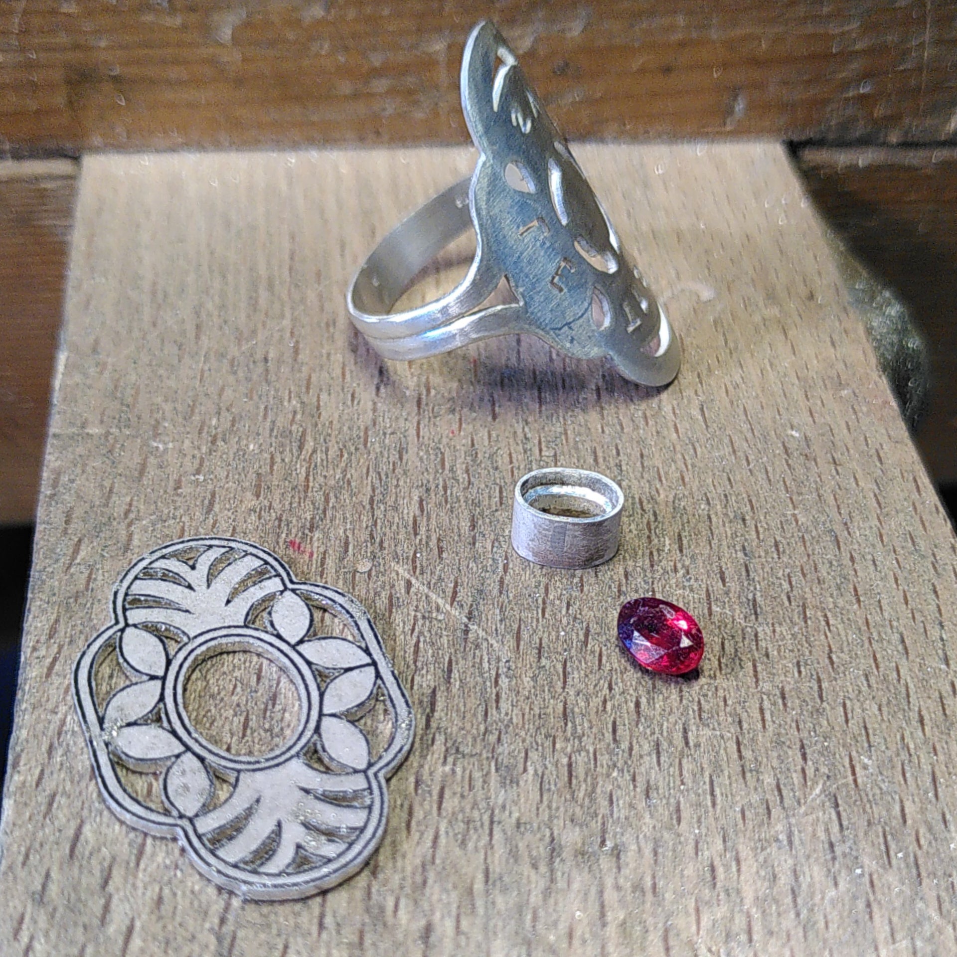 The different silver pieces to be solder to create a Palmier ring, and a red garnet gemstone. Made by hand by Casez Jewellery.