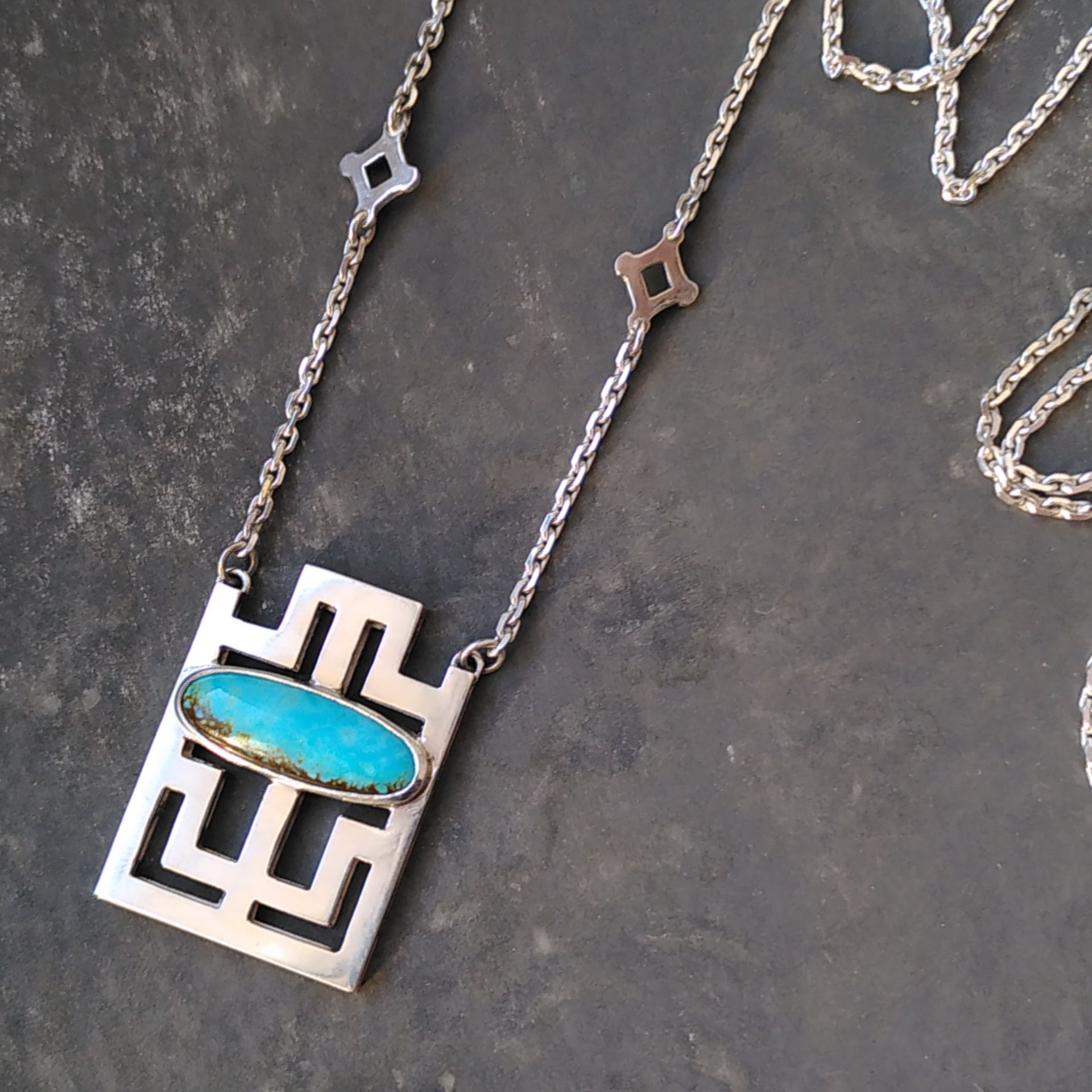 A pendant in the geometric shapes inspired from a key from the middle ages. Displays an oval turquoise cabochon in the middle. Made by hand by CASEZ Jewellery.
