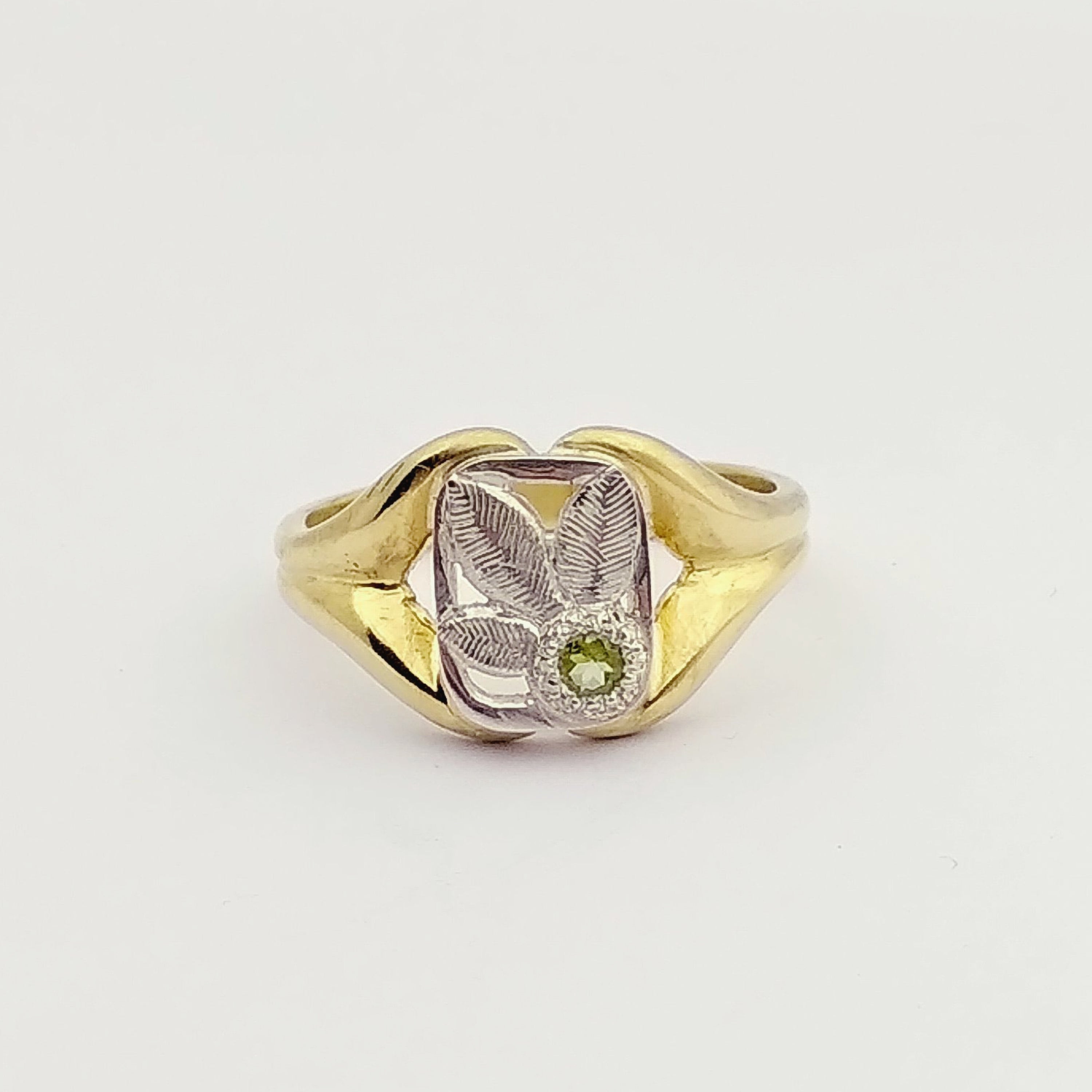 A gold ring with a silver top engraved in the shape of three leaves, with a small peridot gemtsone. Made by hand by Casez Jewellery.