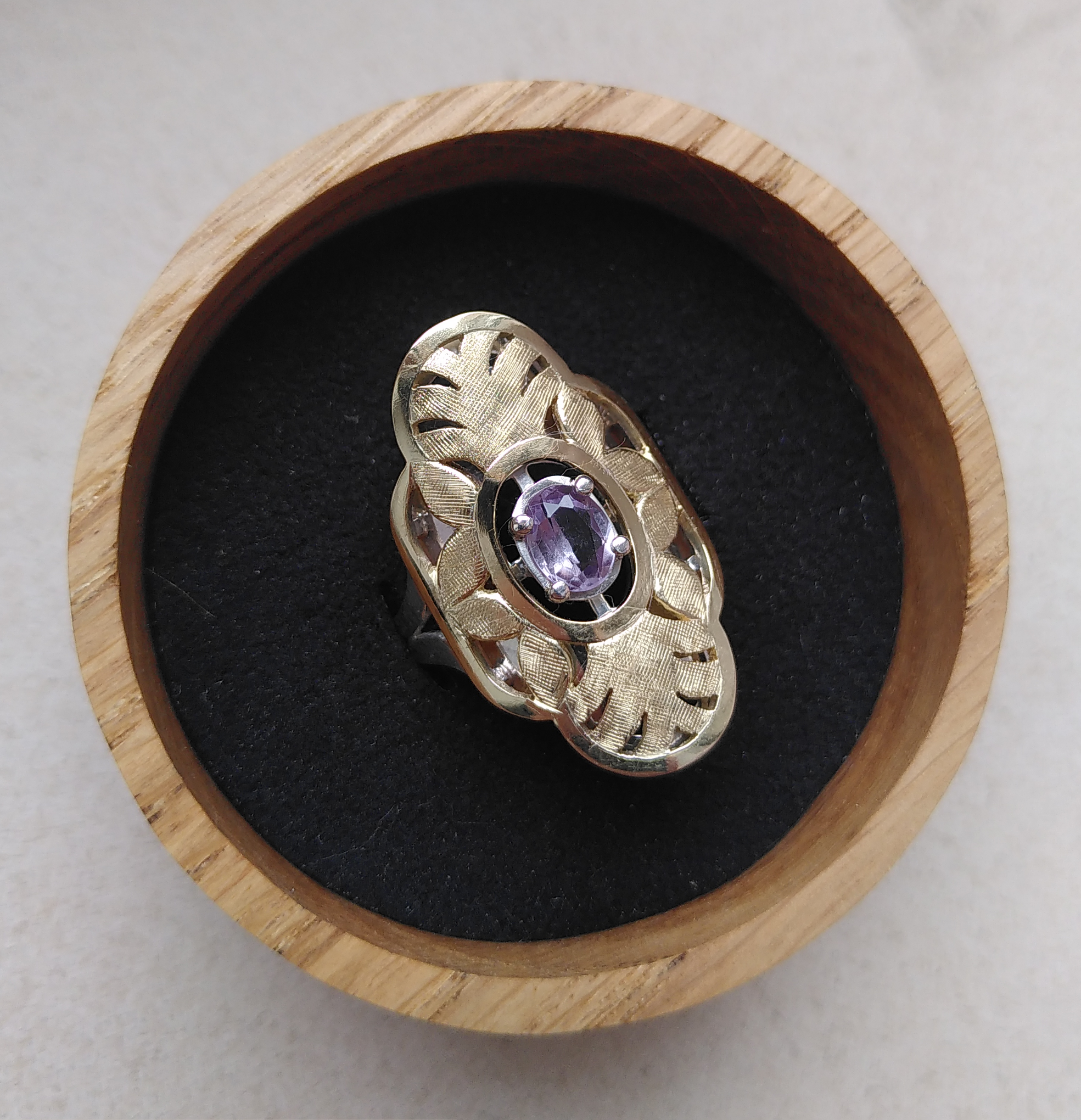 A gold and silver ring. The top plate displays a hand engraved pattern of palm tree leaves and normal leaves. In the middle, a synthetic sapphire is set. The stone is purple under yellow light and turns green under sunlight. Made by hand by Casez Jewellery.